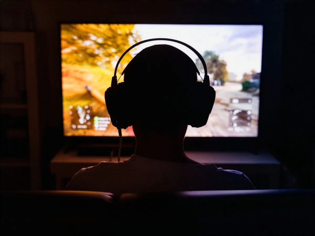 A player in headphones silhouetted against a video game on a TV
